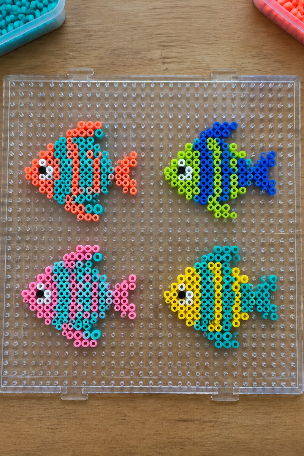 Four colorful perler bead fish designs on a clear pegboard tray.