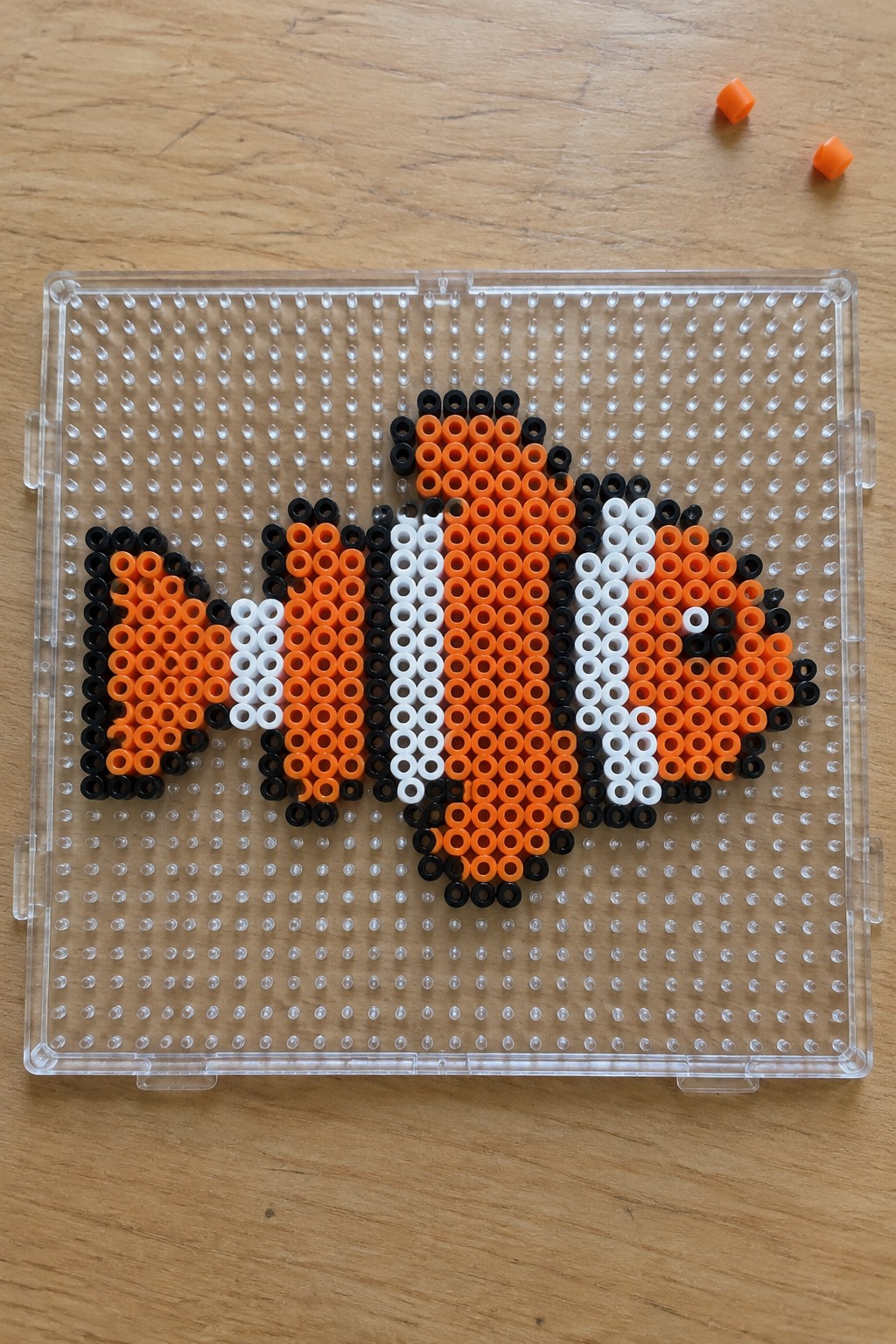 Orange black and white clownfish beads arranged on clear pegboard