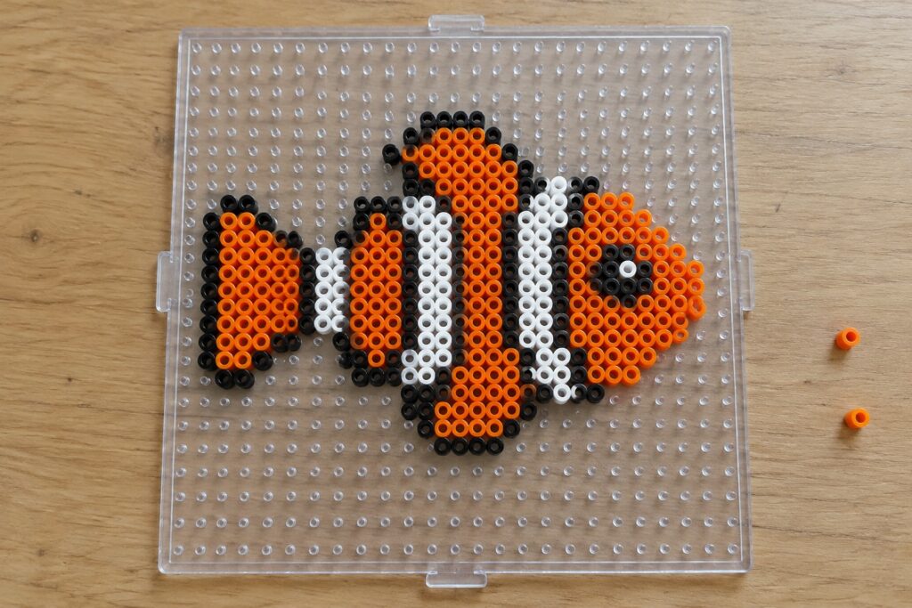 15 Fish Perler Bead Patterns in Bright Ocean Colors Orange black and white clownfish beads arranged on clear pegboard