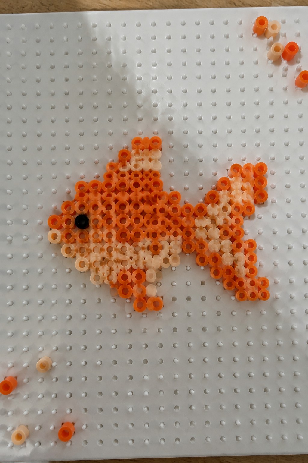 Orange and white beads form a fish on white pegboard with loose beads nearby.
