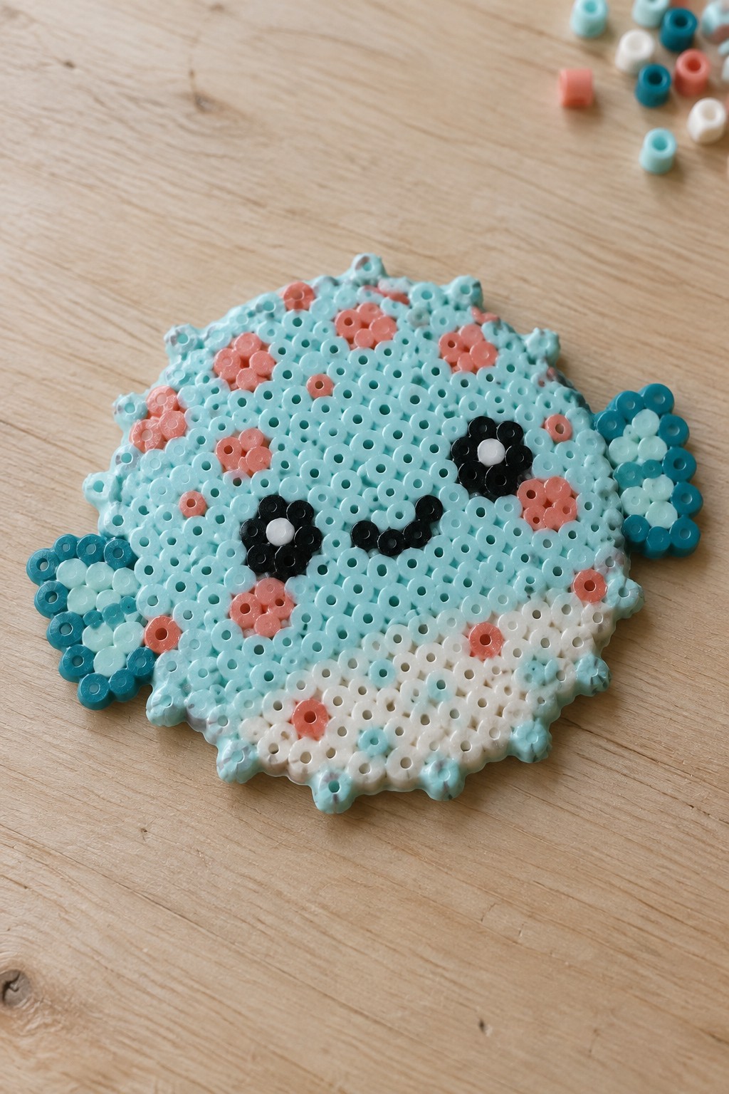 Perler bead blue seal with pink cheeks and smiling face on wood