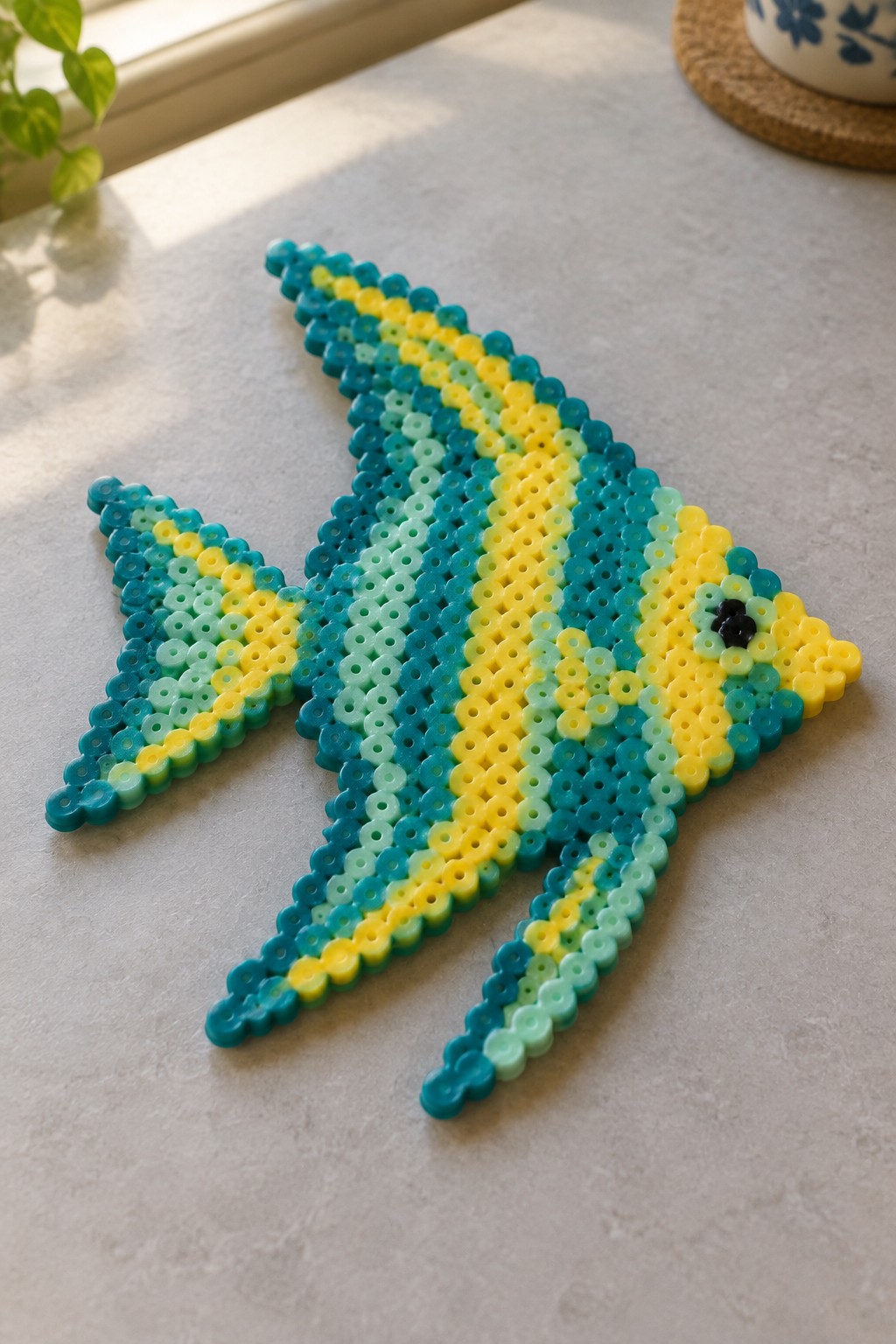 Colorful perler bead fish in blue, yellow, and green on a light table