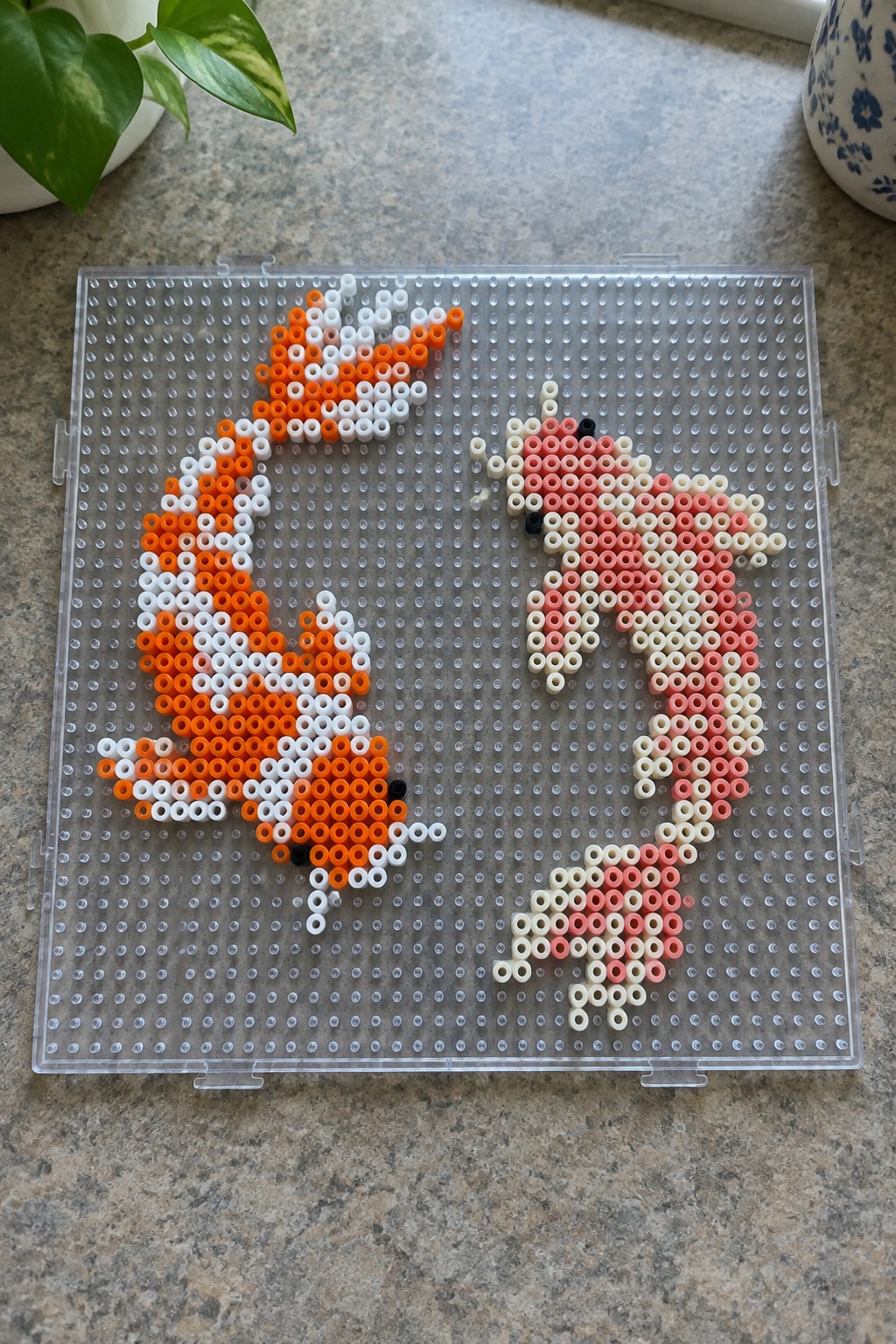 Two perler bead foxes, orange and pink, on a clear pegboard tray