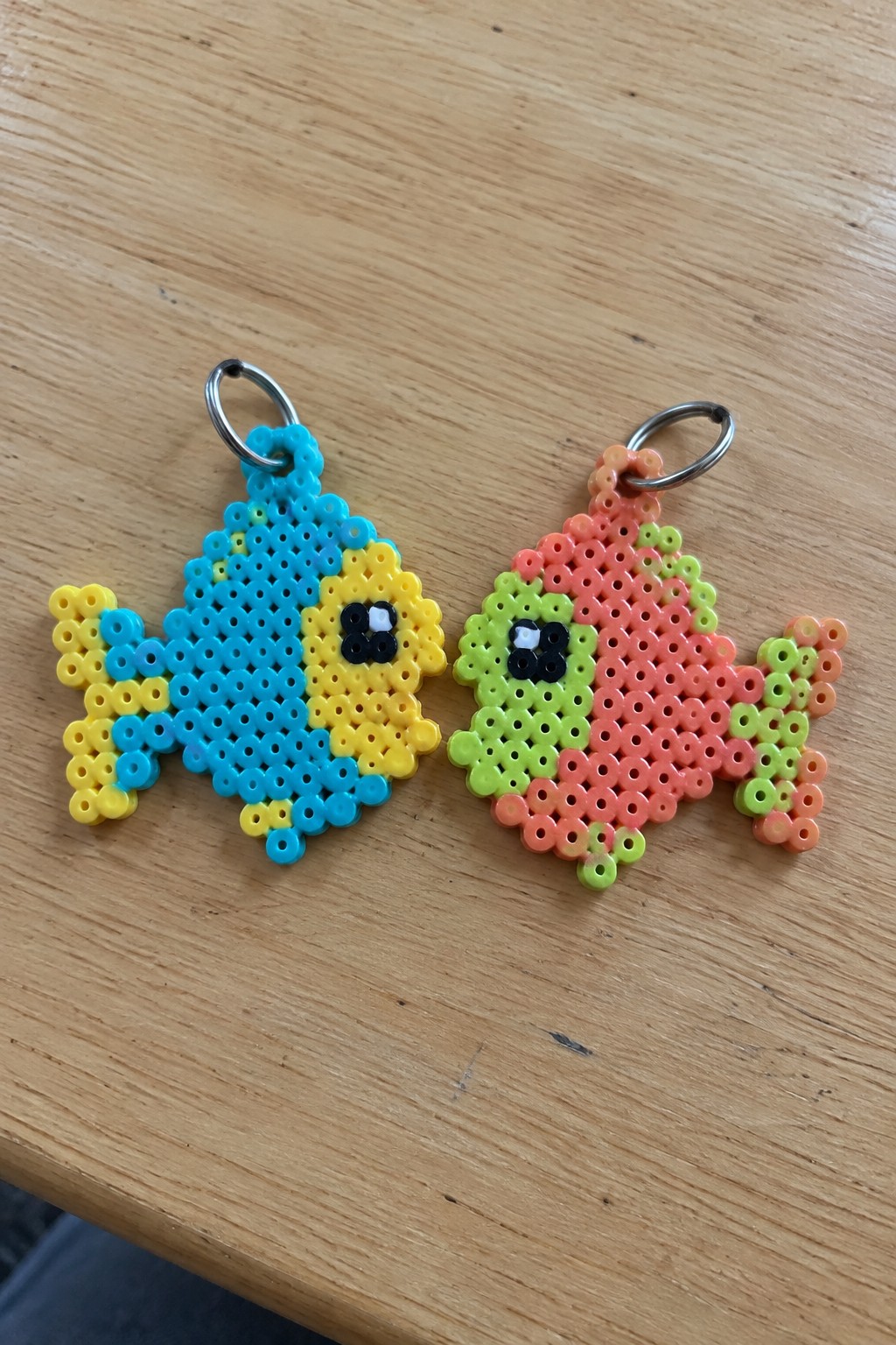 Two colorful perler bead fish keychains on a wooden table.