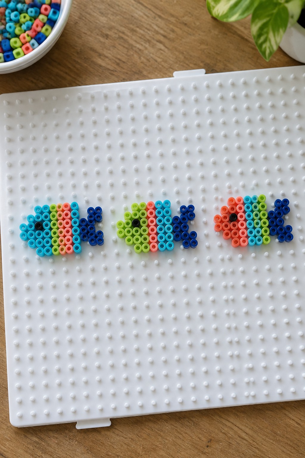 Three fish Perler bead patterns in bright colors on a white pegboard.