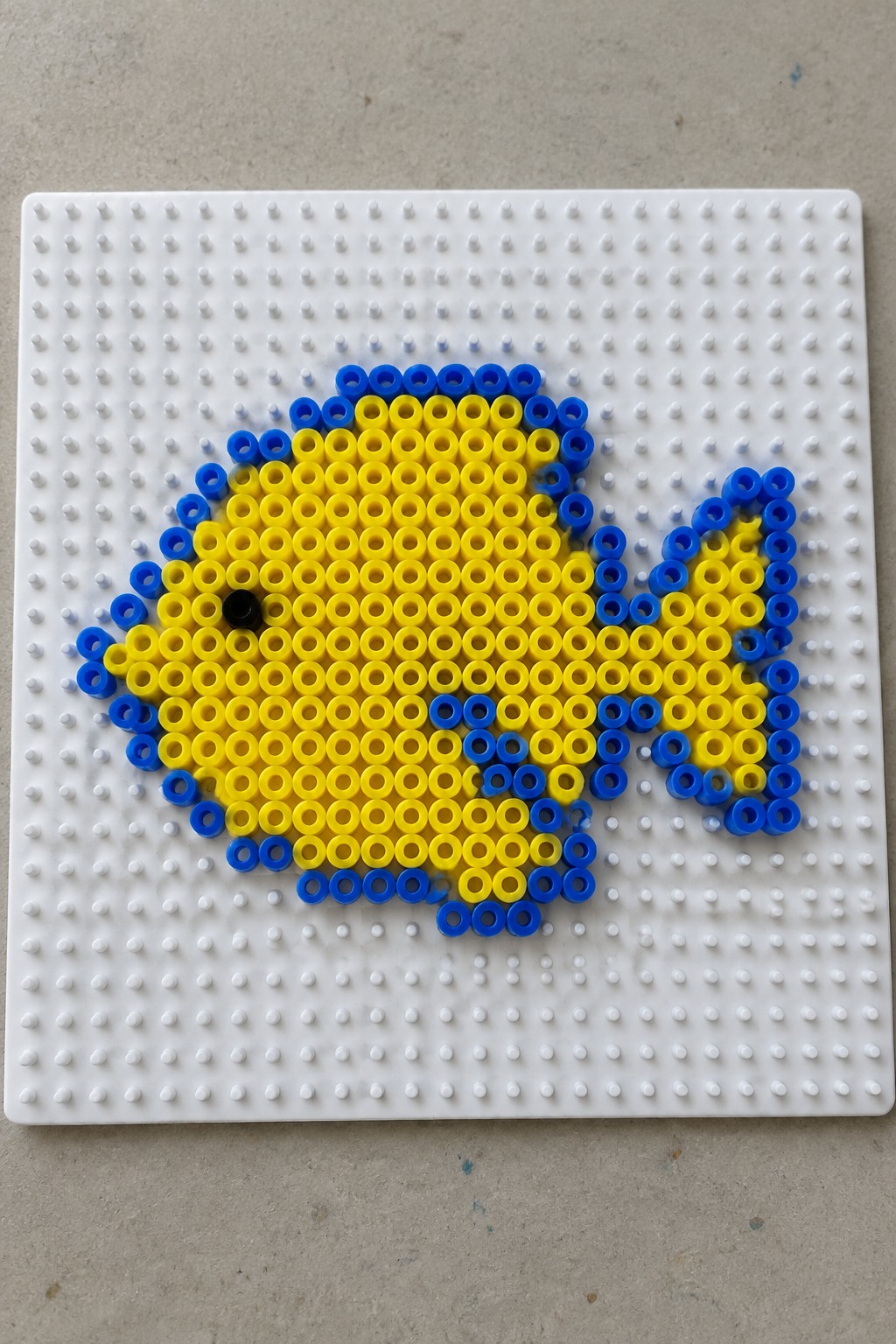Yellow and blue perler bead fish with black eye on white pegboard
