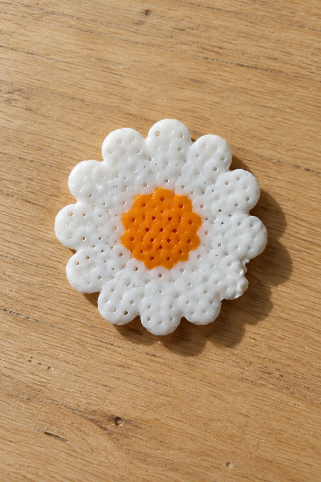 White and orange beaded daisy flower craft on wooden surface