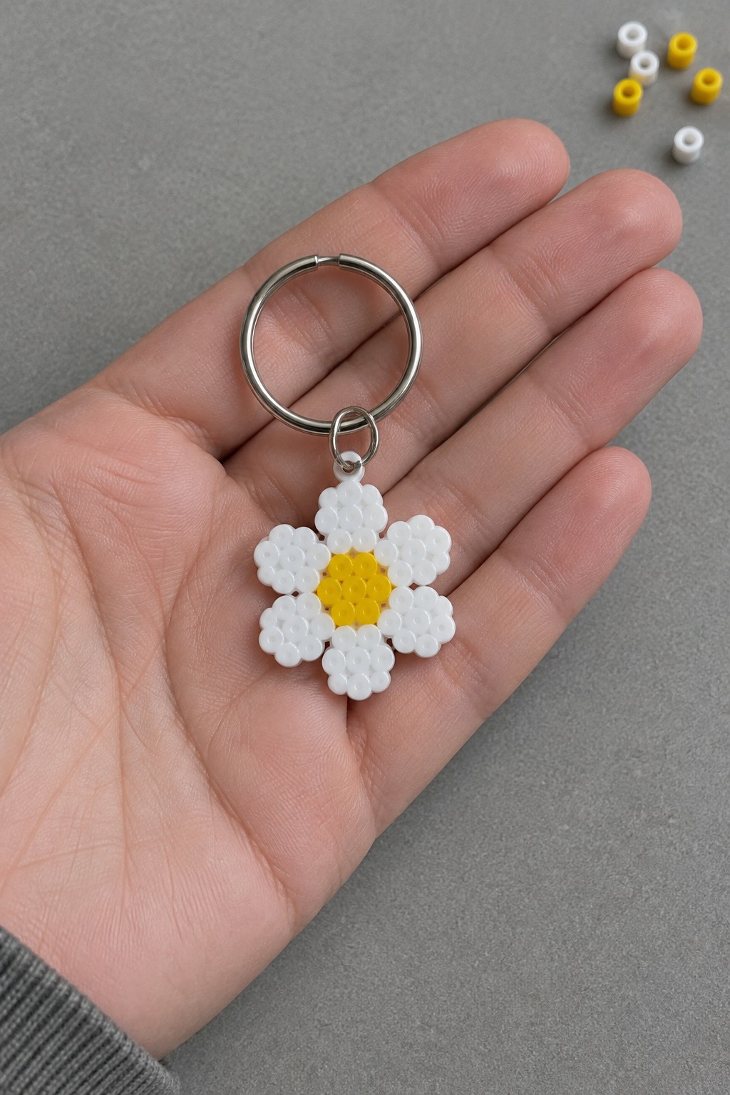 Hand holding daisy keychain of white and yellow perler beads with silver ring