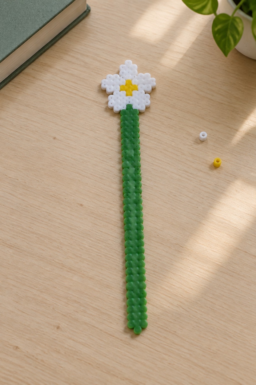 White daisy with yellow center and green stem made from perler beads on wood