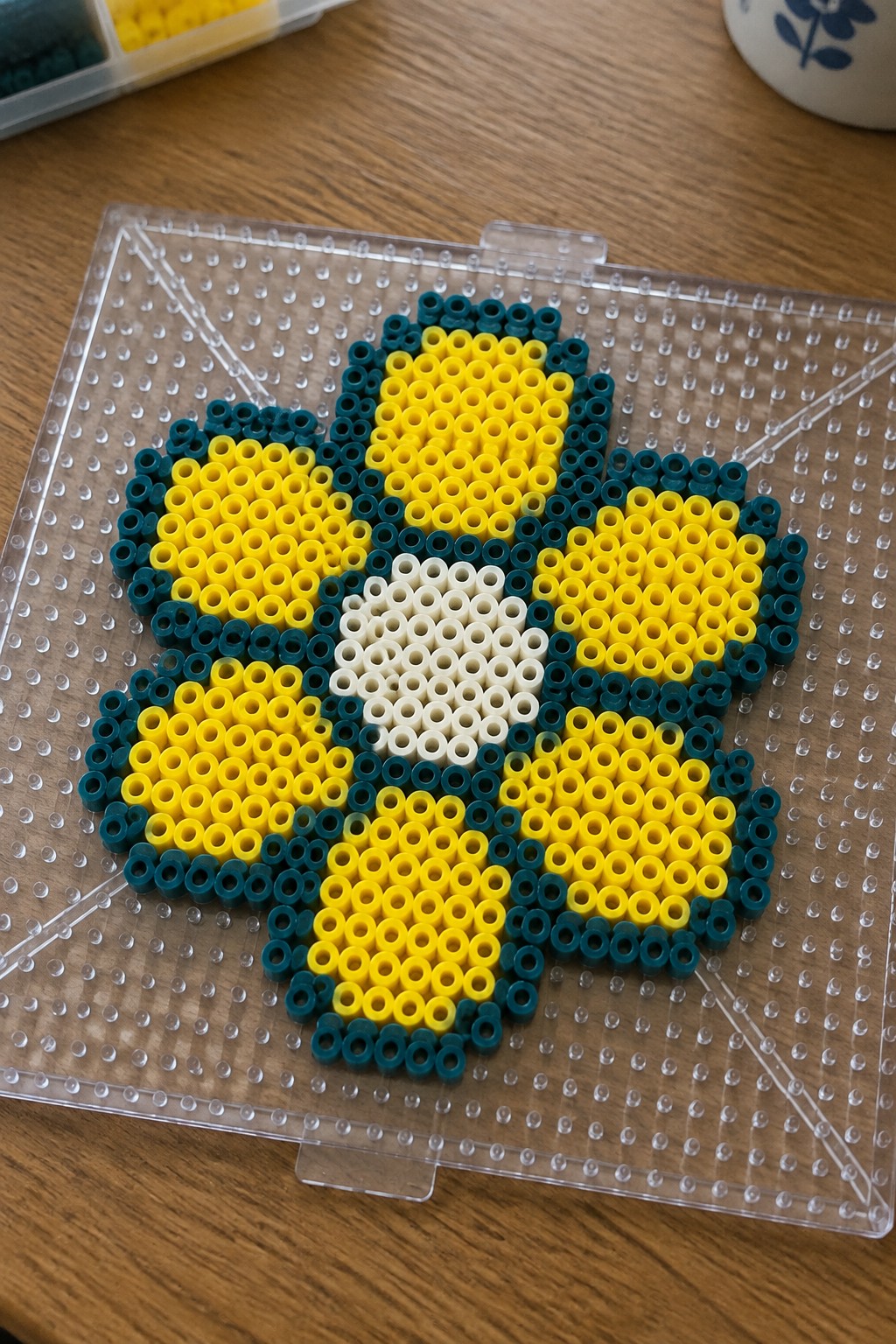 Yellow and teal perler bead flower with white center on clear pegboard