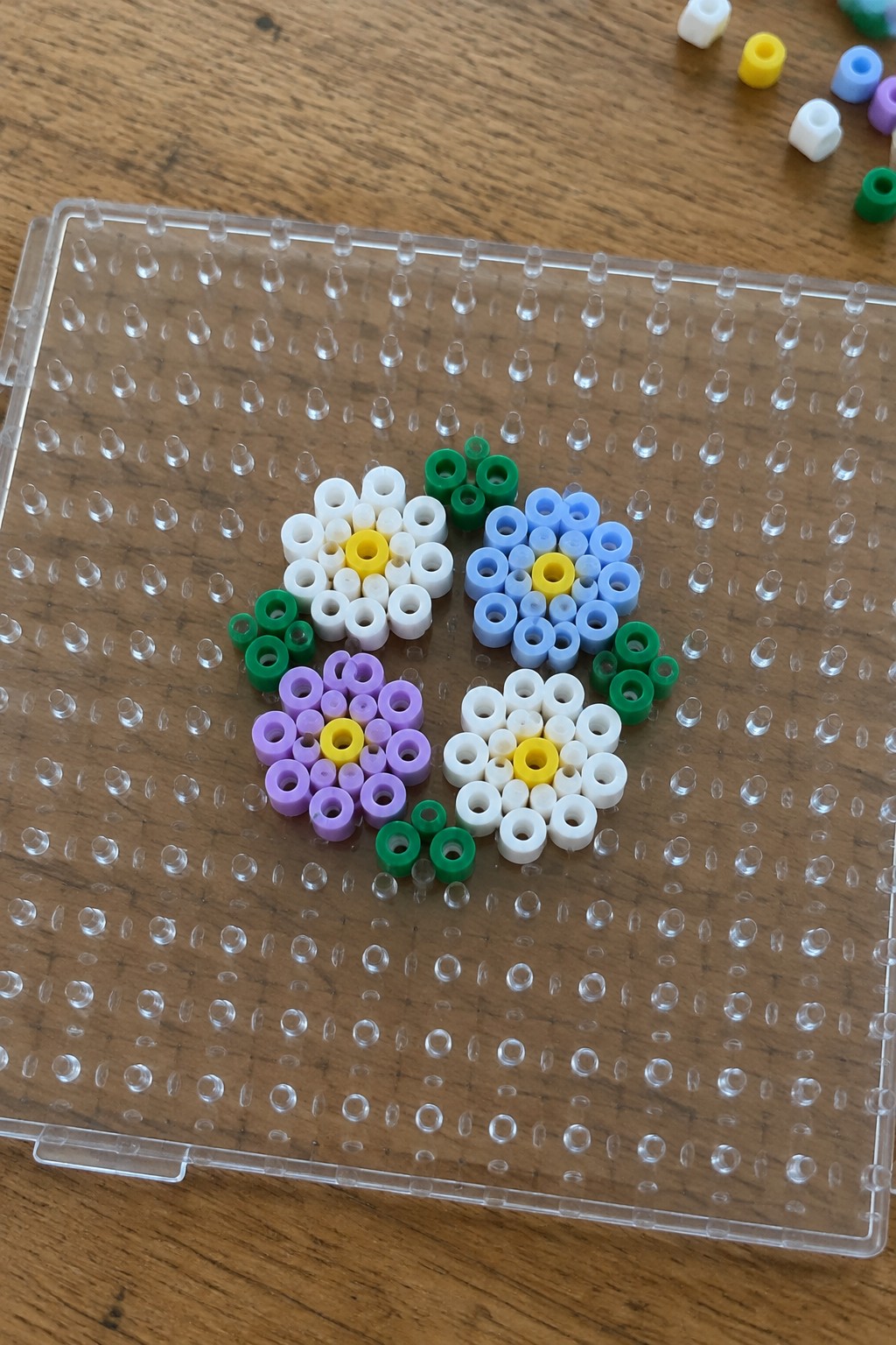 Colorful perler bead flowers arranged on a clear pegboard over wood