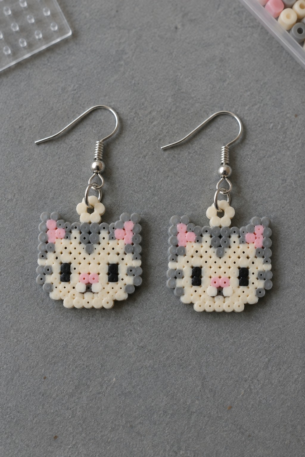 Two matching fused Perler bead cat face earrings with gray, white, pink, and black beads on silver hooks.