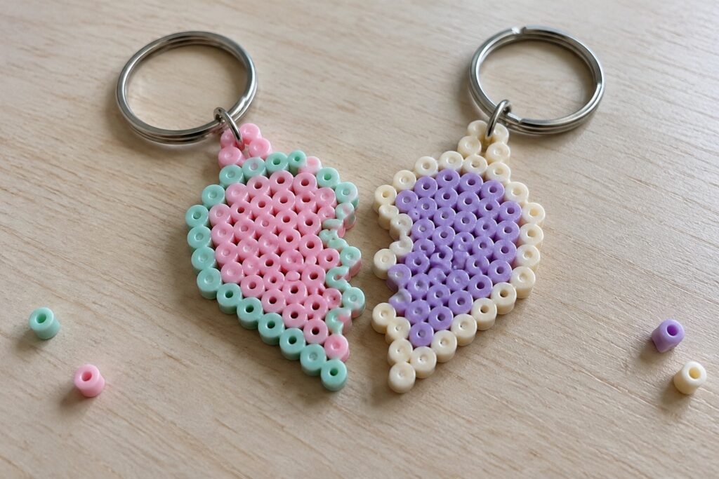 16 Friendship Fuse Bead Crafts for Matching Handmade Gifts Two fused Perler bead keychains with matching angular shapes, one in pink and mint green, the other in purple and cream, attached to metal rings.