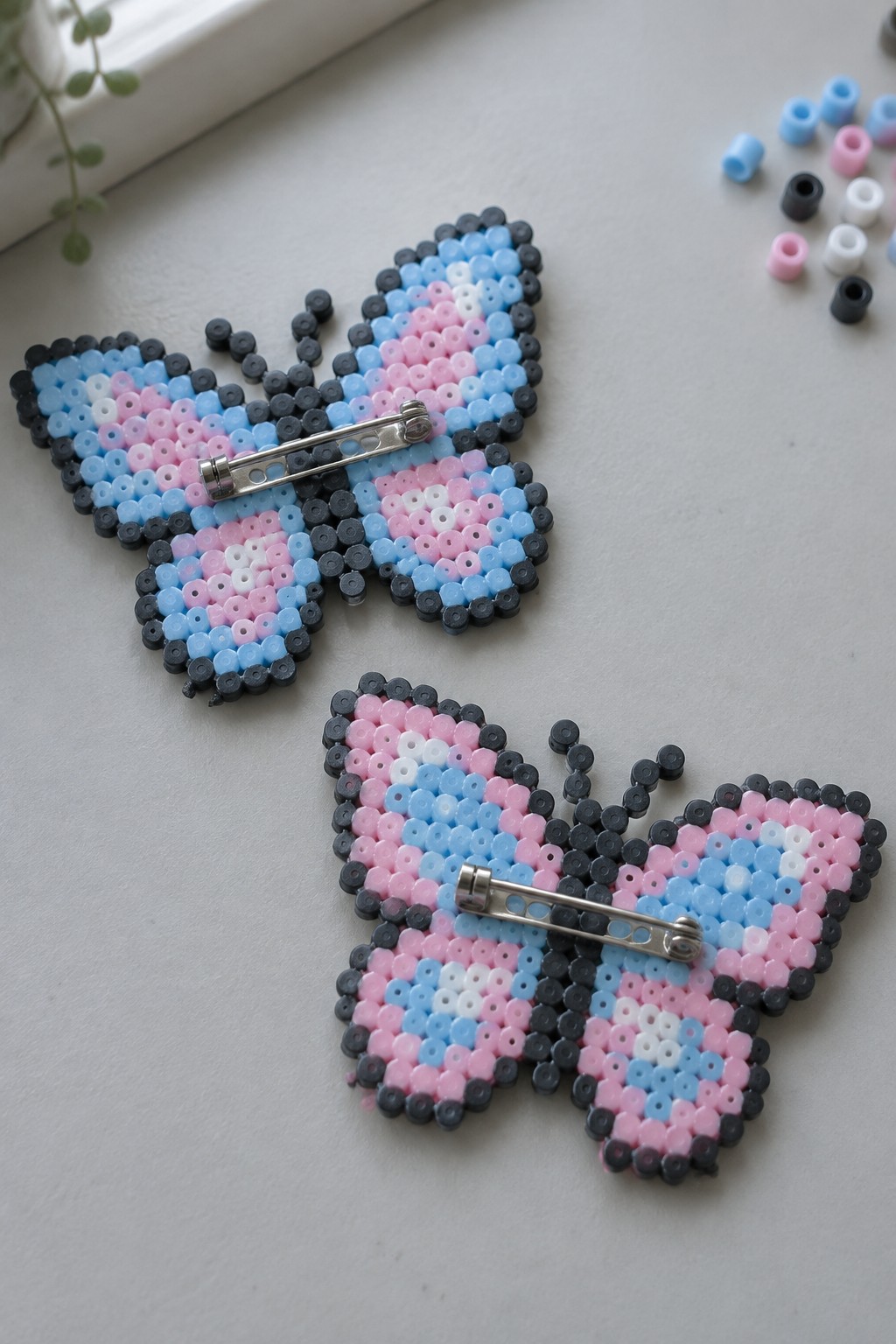 Two perler bead butterflies in pink blue white with safety pin backs