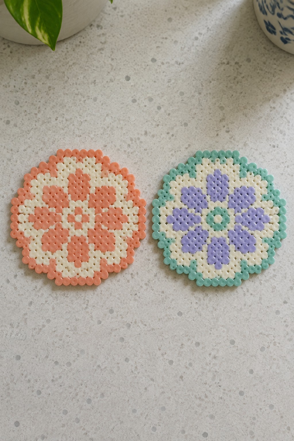 Two perler bead coasters with floral patterns in peach, purple, and mint.