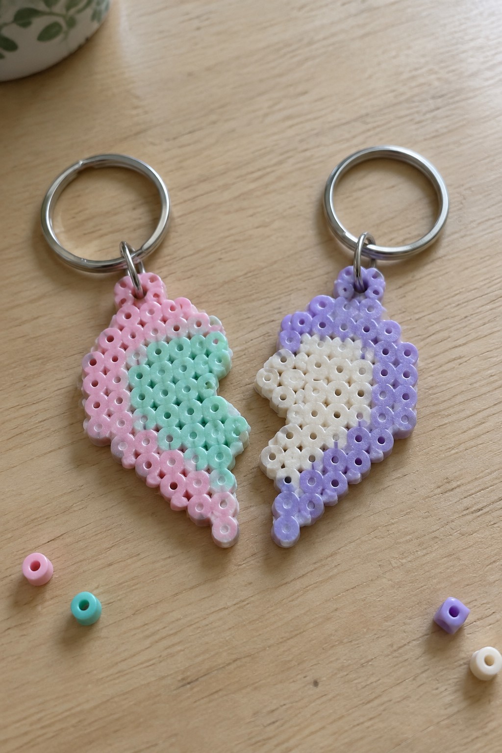 Two fused Perler bead keychains with matching angular shapes, one in pink and mint green, the other in purple and cream, attached to metal rings.