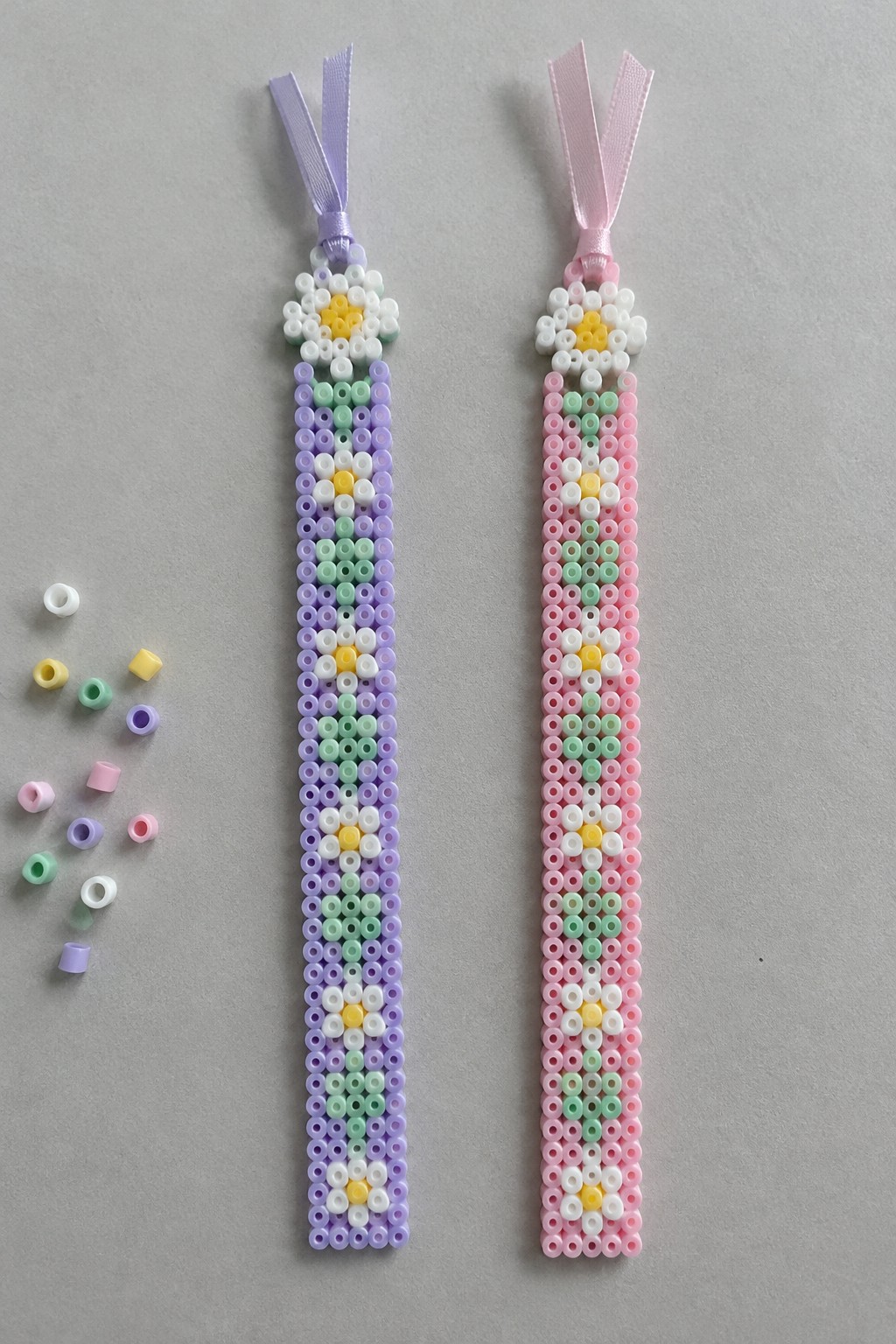 Two daisy-patterned beaded straps in purple and pink with ribbons and loose beads.