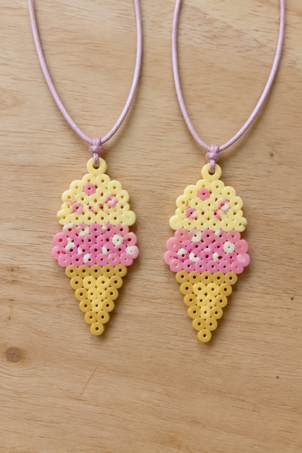 Two pink and yellow perler bead ice cream cone necklaces on wood.
