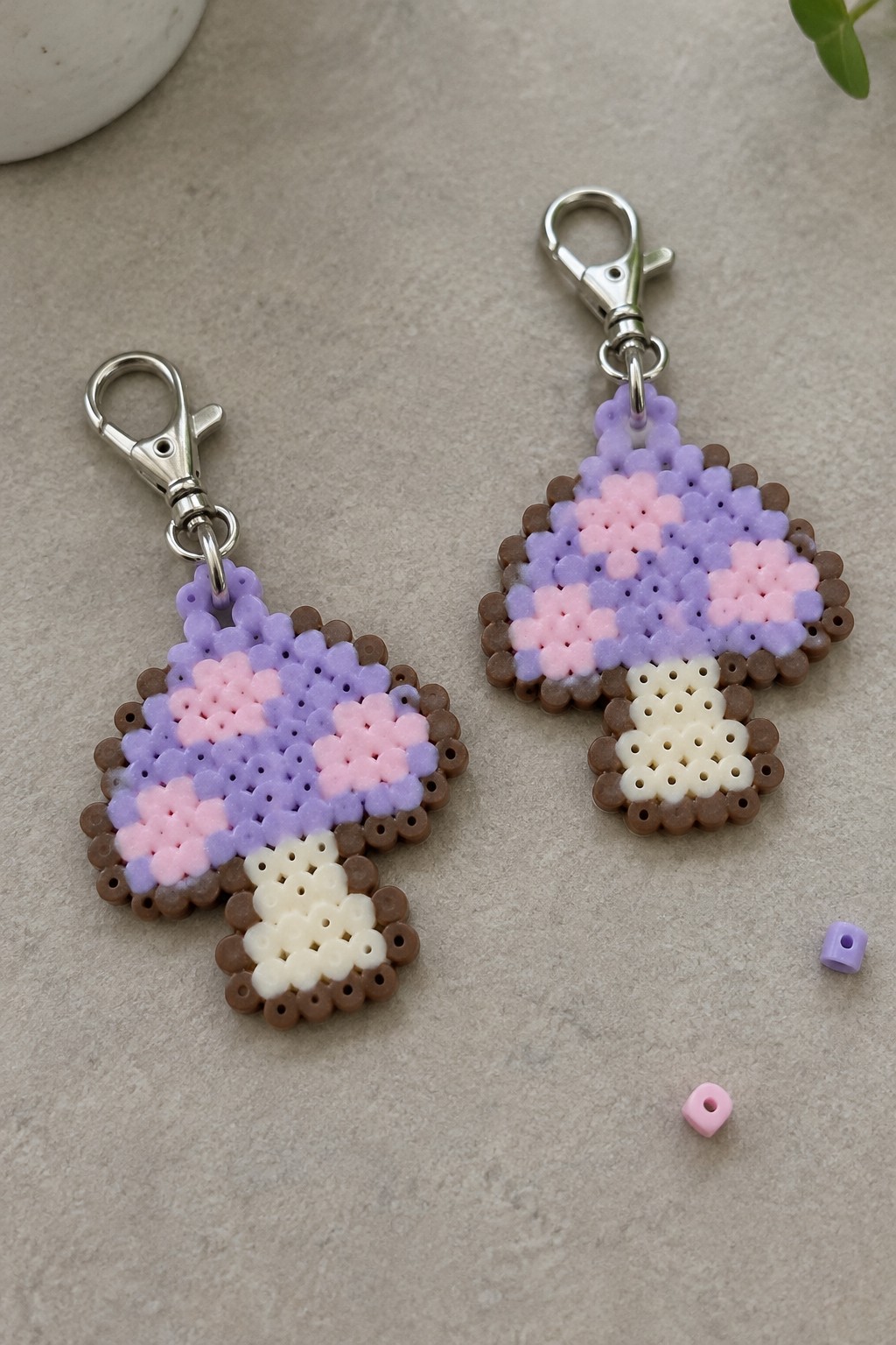 Two pastel perler bead mushroom keychains with silver clasps on gray surface.