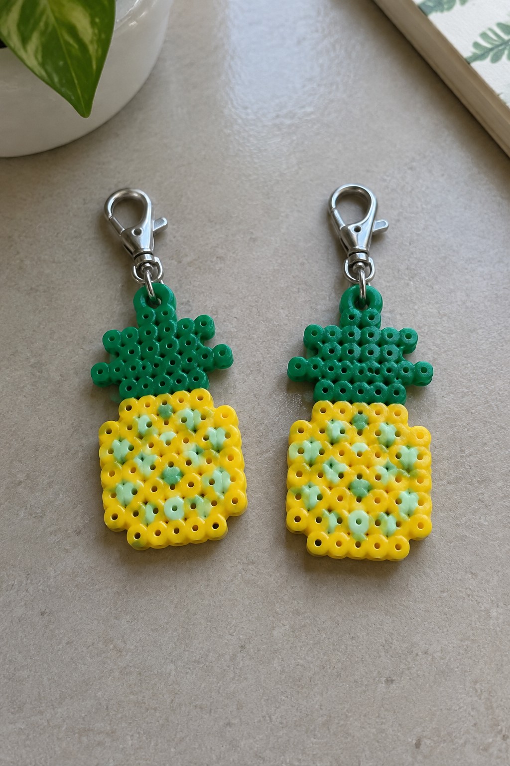 Two perler bead pineapple keychains with green tops, yellow bodies, and silver clasps.