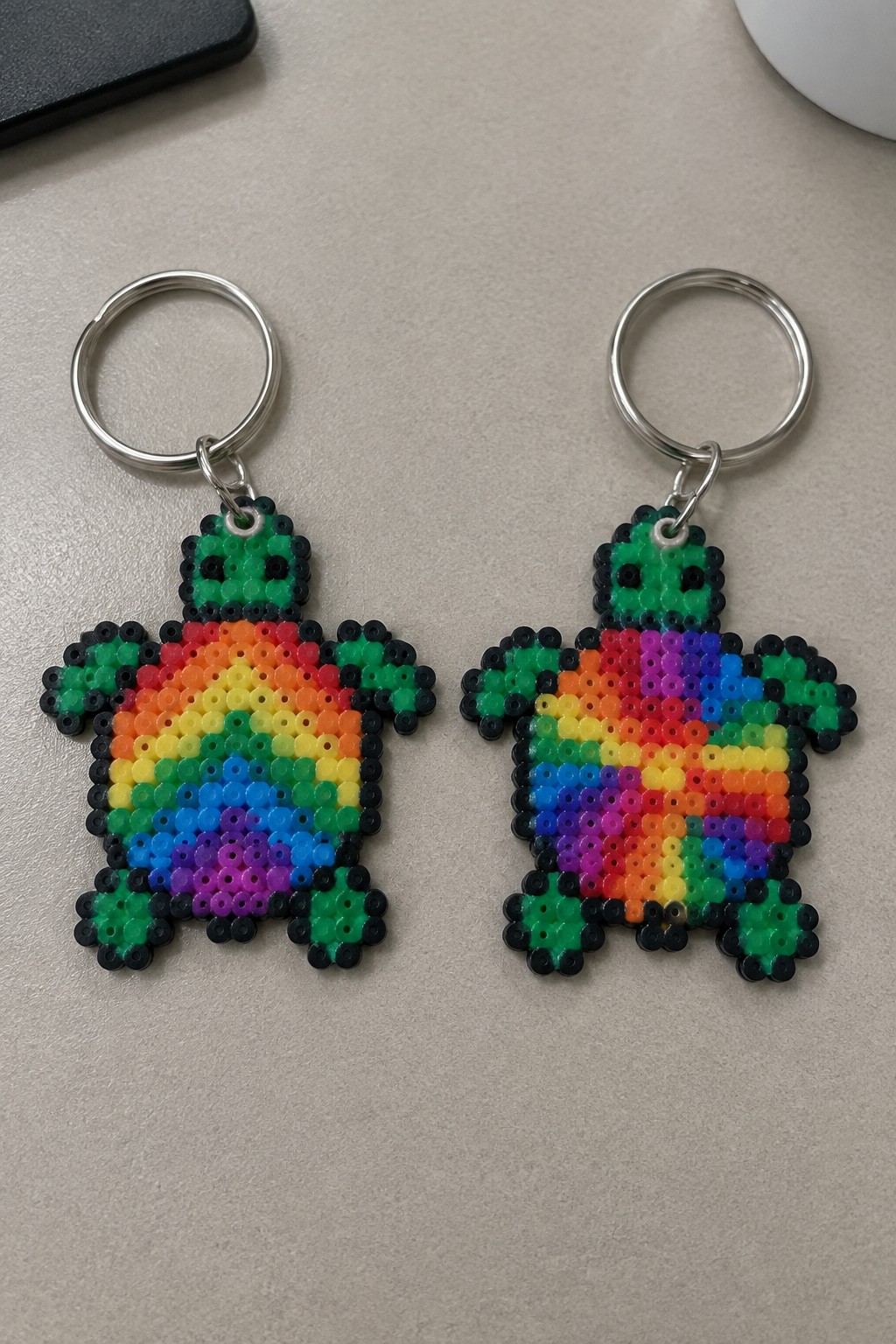 Two rainbow perler bead turtle keychains with green heads and silver rings