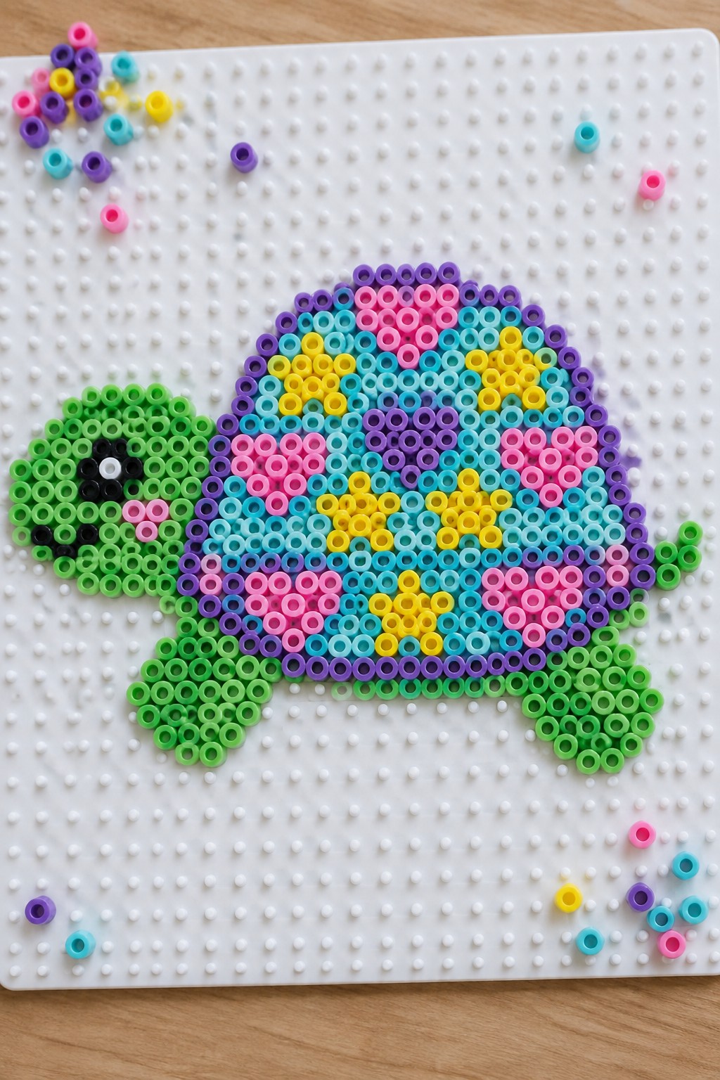Rainbow turtle Perler bead pattern on a pegboard with green head and multicolored shell.