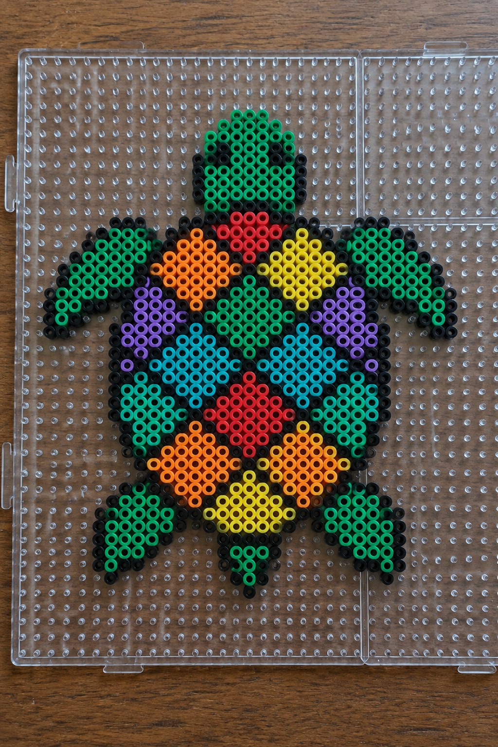 Perler bead turtle with rainbow shell colors arranged on a clear pegboard.