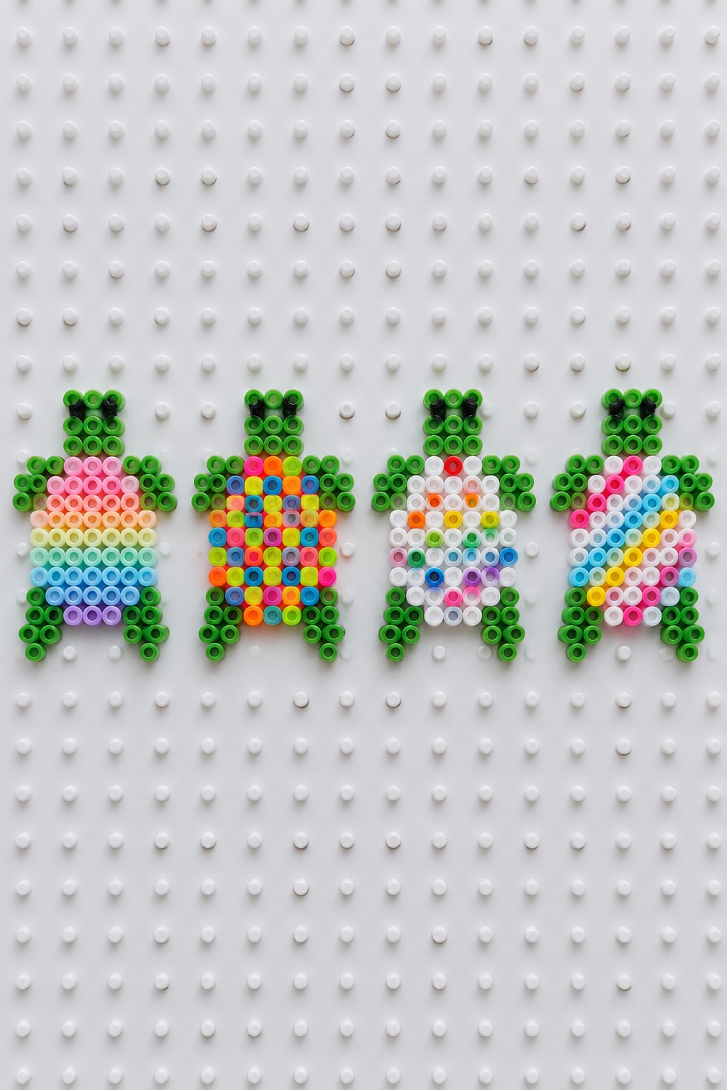 Four colorful beaded turtles with rainbow shells on a white pegboard.