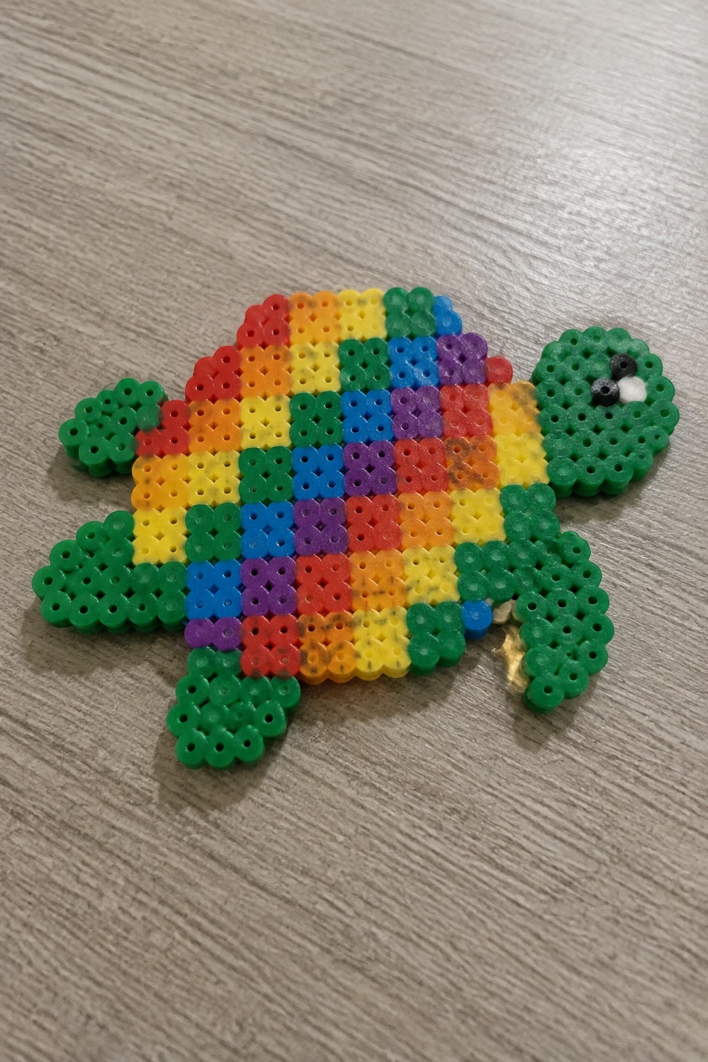 Perler bead turtle with rainbow striped shell and green head and limbs arranged on a pegboard.
