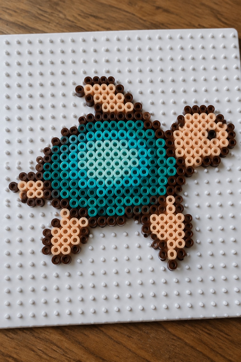 Perler bead turtle with brown limbs and gradient turquoise shell on white pegboard