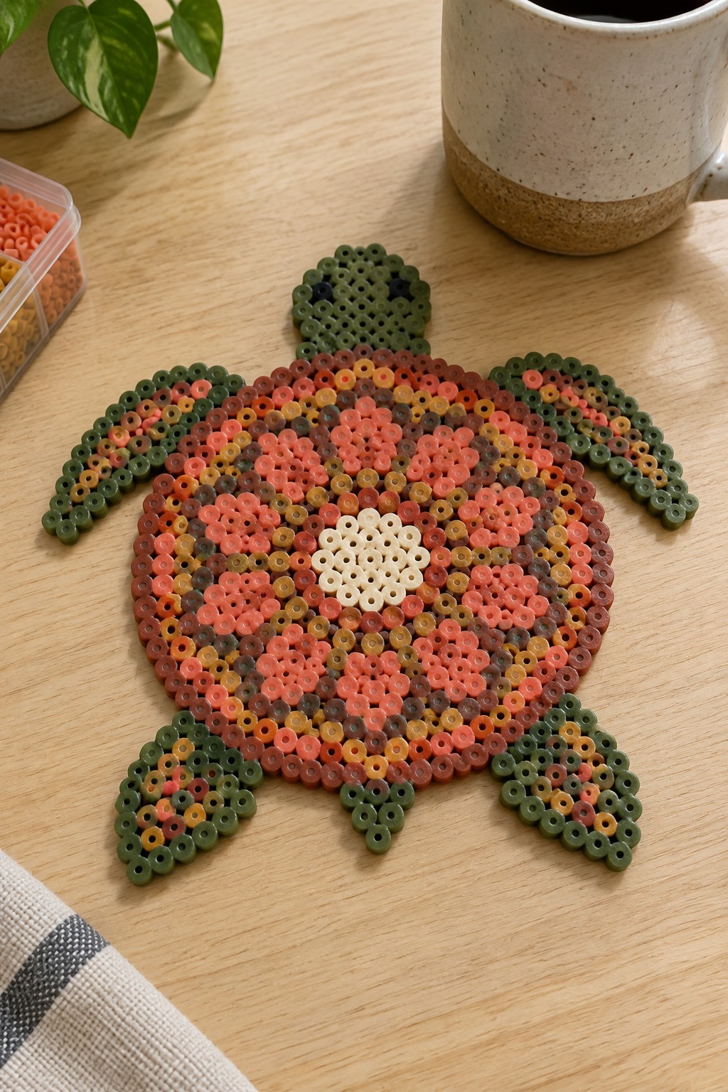 Colorful perler bead turtle with white center on wooden table beside mug and plant