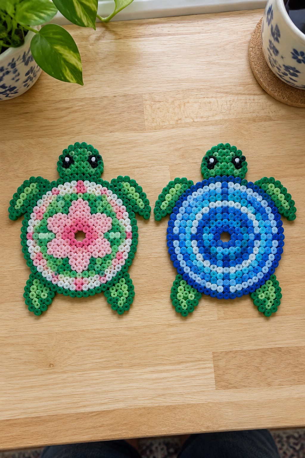 Two Perler bead turtles on a table, one with a pink and green ringed shell and the other with a blue gradient shell.
