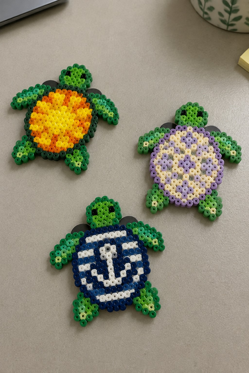 Three perler bead turtles with green bodies and yellow, purple, blue patterned shells.