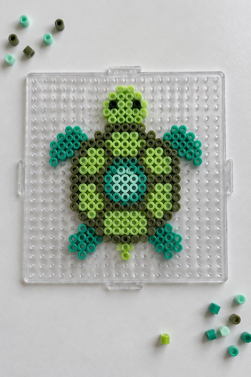 Green Perler bead turtle on clear pegboard with scattered loose beads around