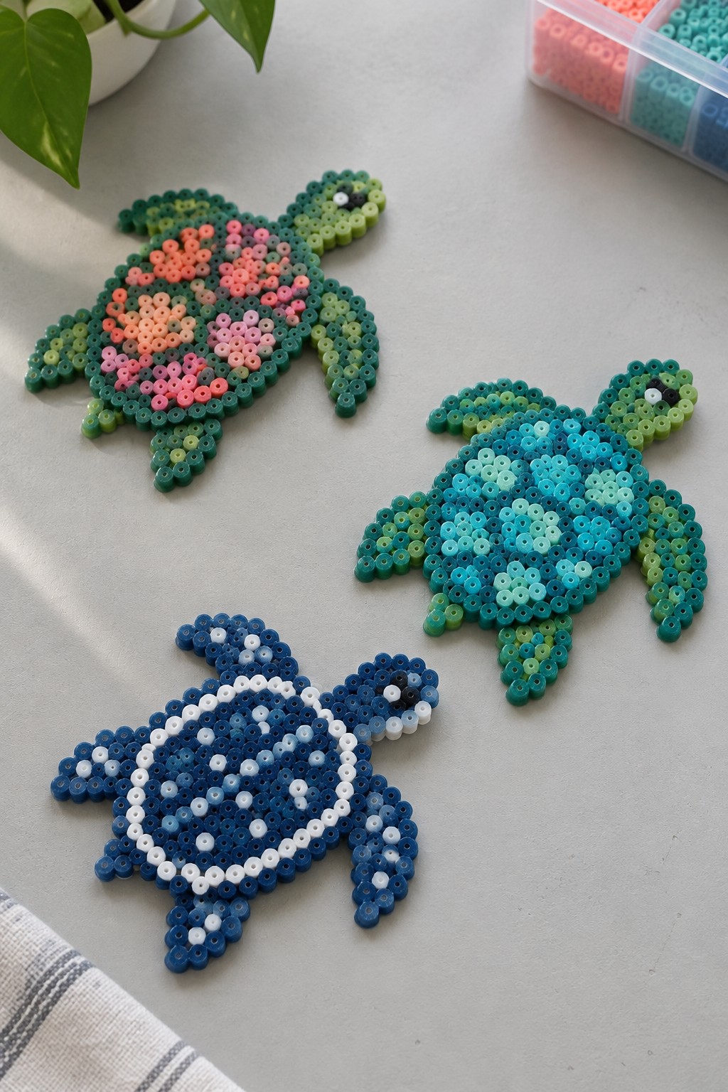 Three perler bead turtles with floral, wave, and ocean patterns on gray surface