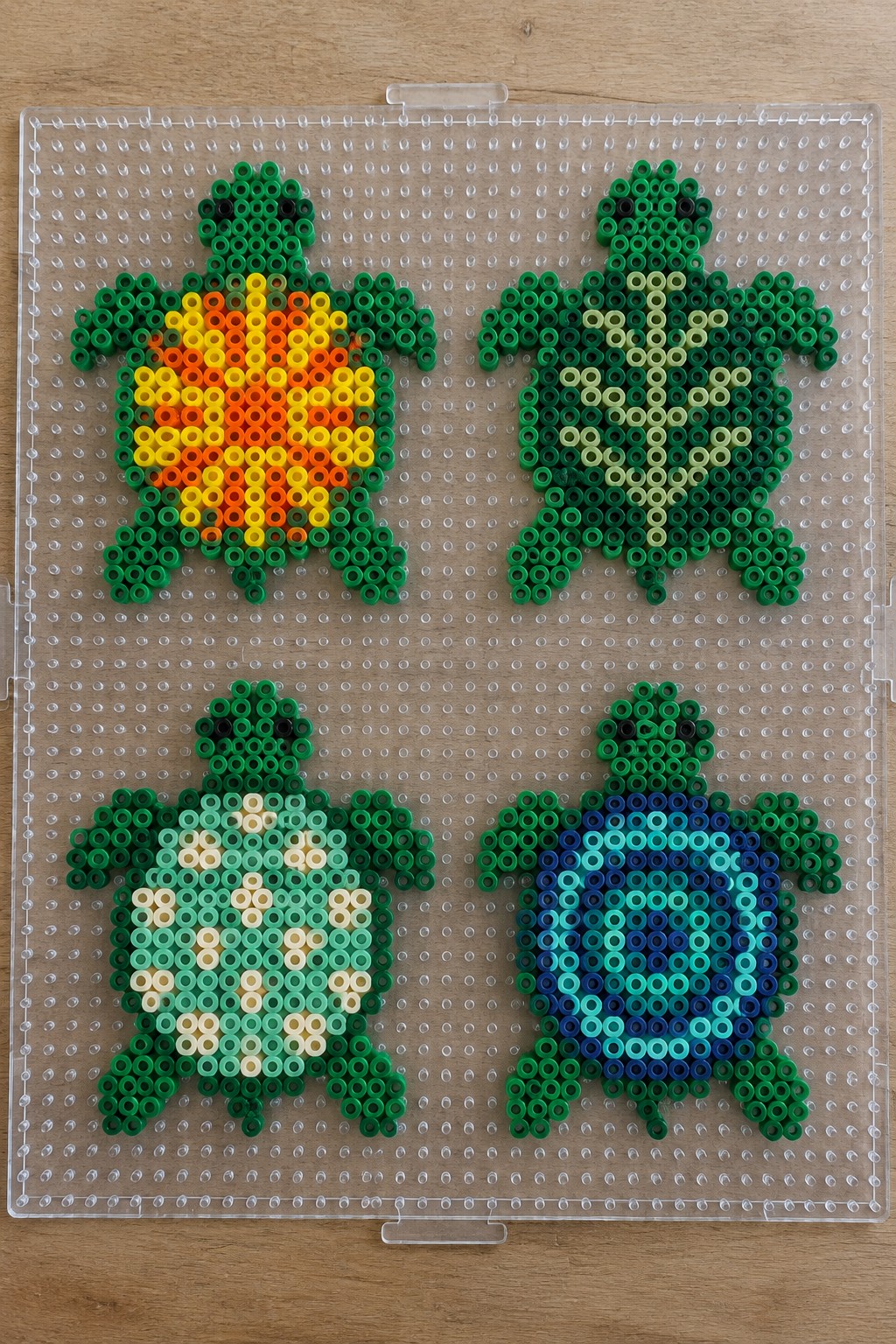 Four perler bead turtles with colorful patterned shells on clear pegboard