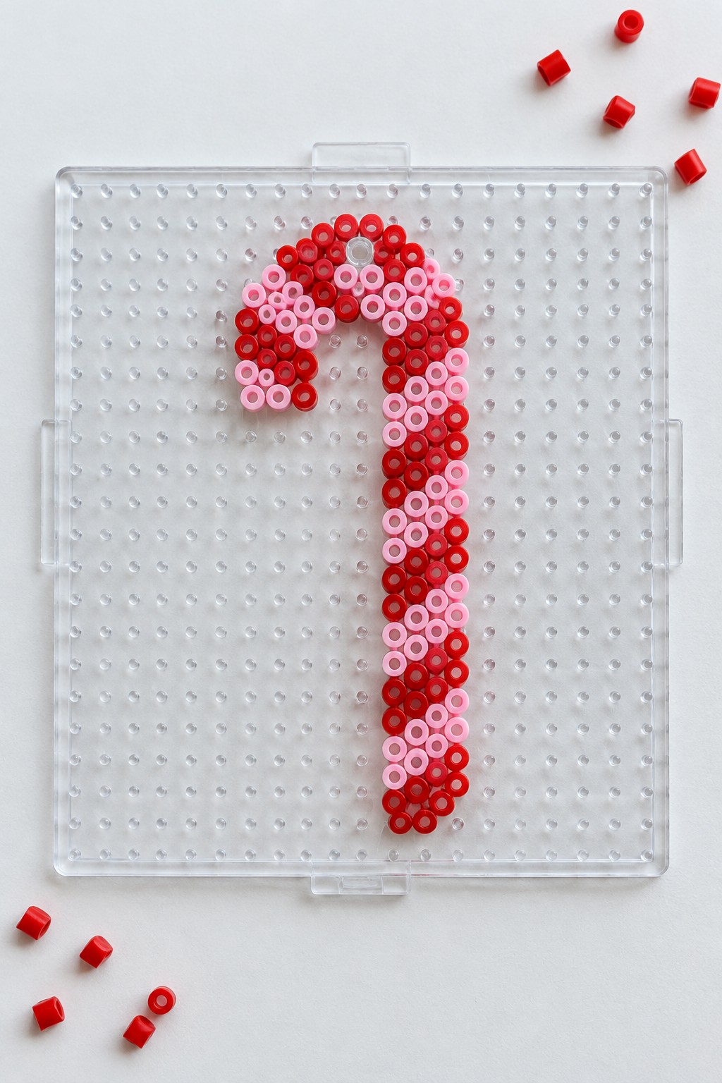 Red and pink beaded candy cane on clear pegboard with loose red beads nearby
