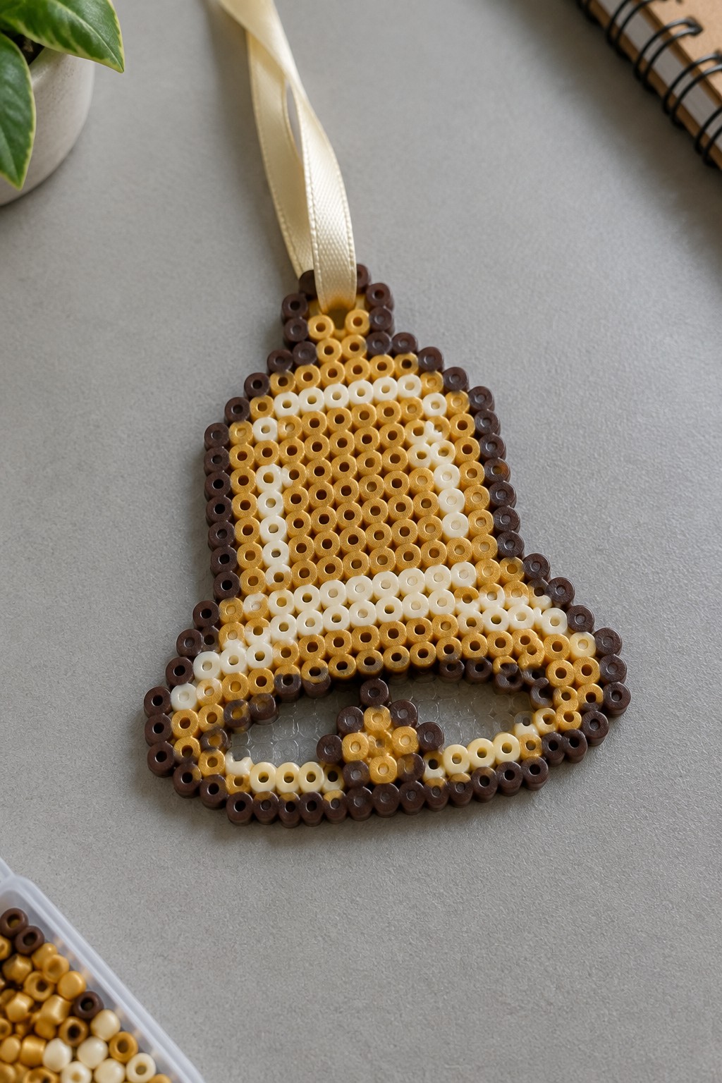 Perler bead Christmas bell ornament in brown, yellow, and white with ribbon.