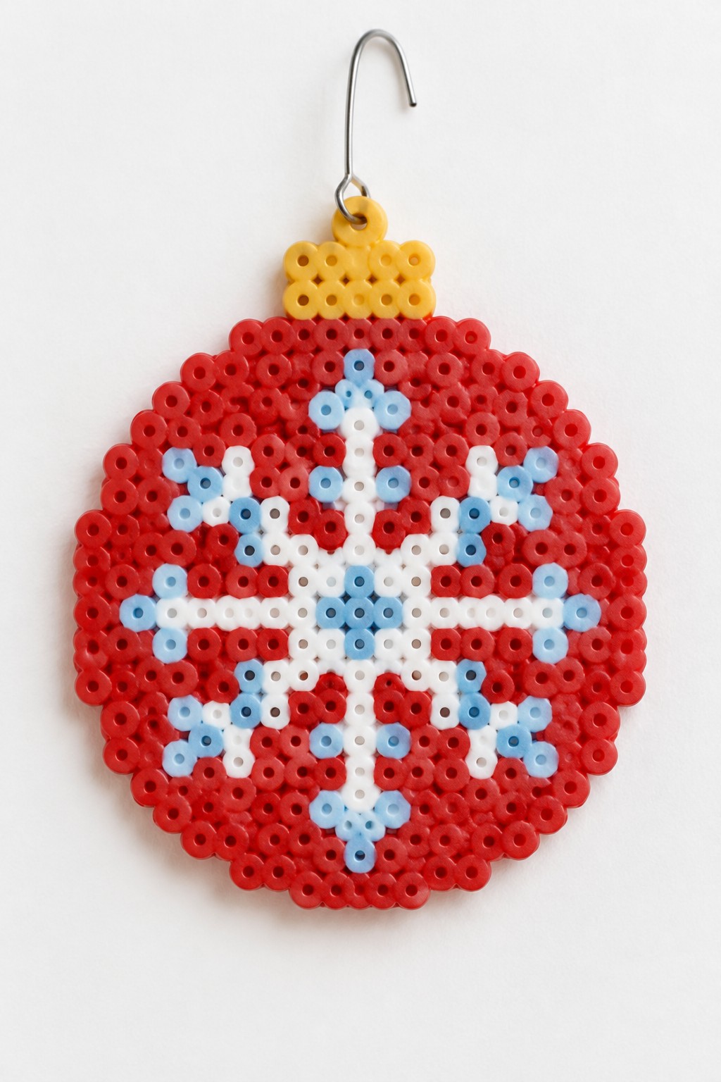 Red perler bead Christmas ornament with white snowflake and yellow hanging hook.