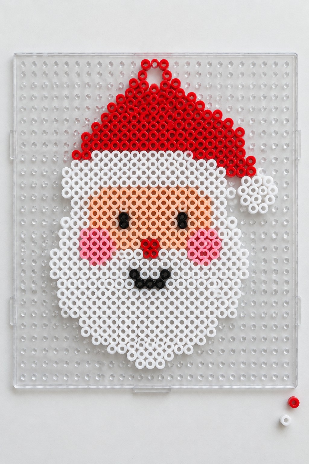 Perler bead Santa face on clear pegboard with red hat and white beard
