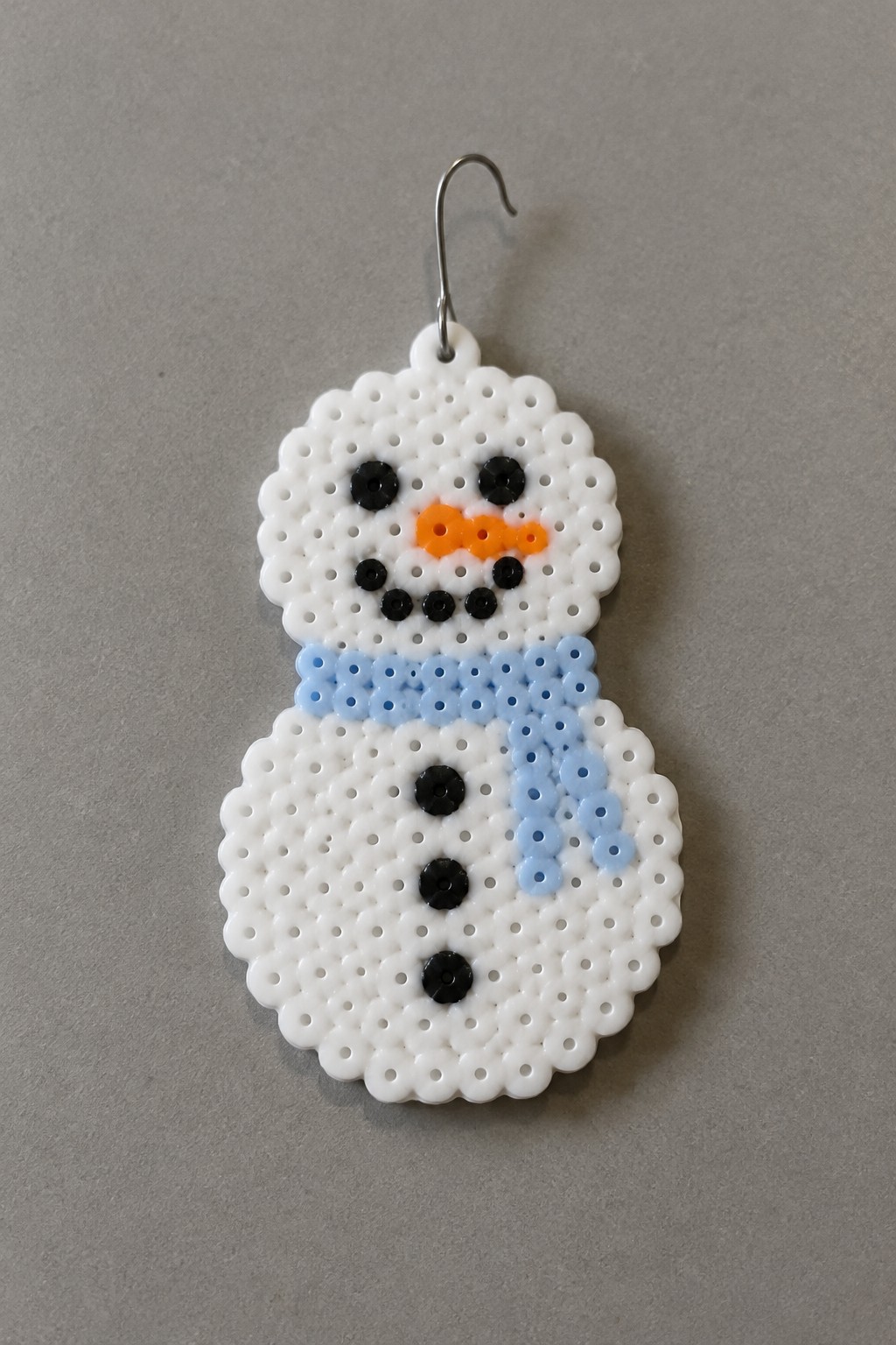White perler bead snowman earring with black eyes, orange nose, and blue scarf.