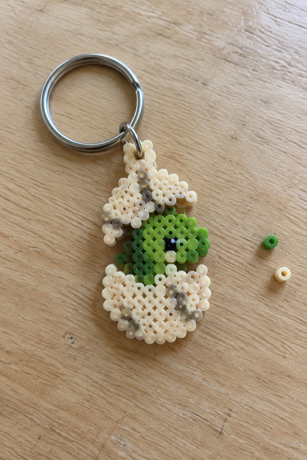 Perler bead keychain with green pixelated character and metal ring on wood