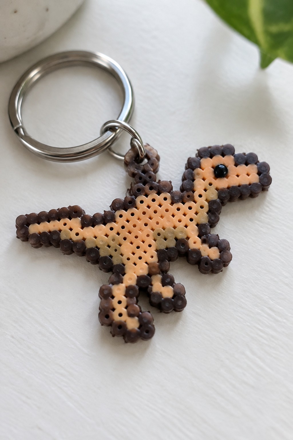 Metal keyring with brown and peach perler bead lizard keychain on white surface
