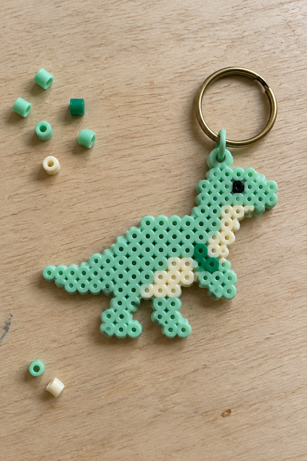 Mint green perler bead dinosaur keychain with gold ring and scattered beads