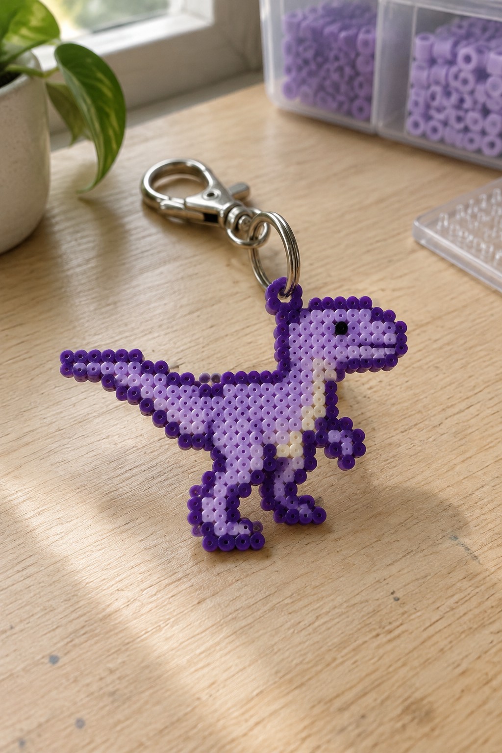 A fused Perler bead keychain shaped like a purple dinosaur attached to a metal clasp.