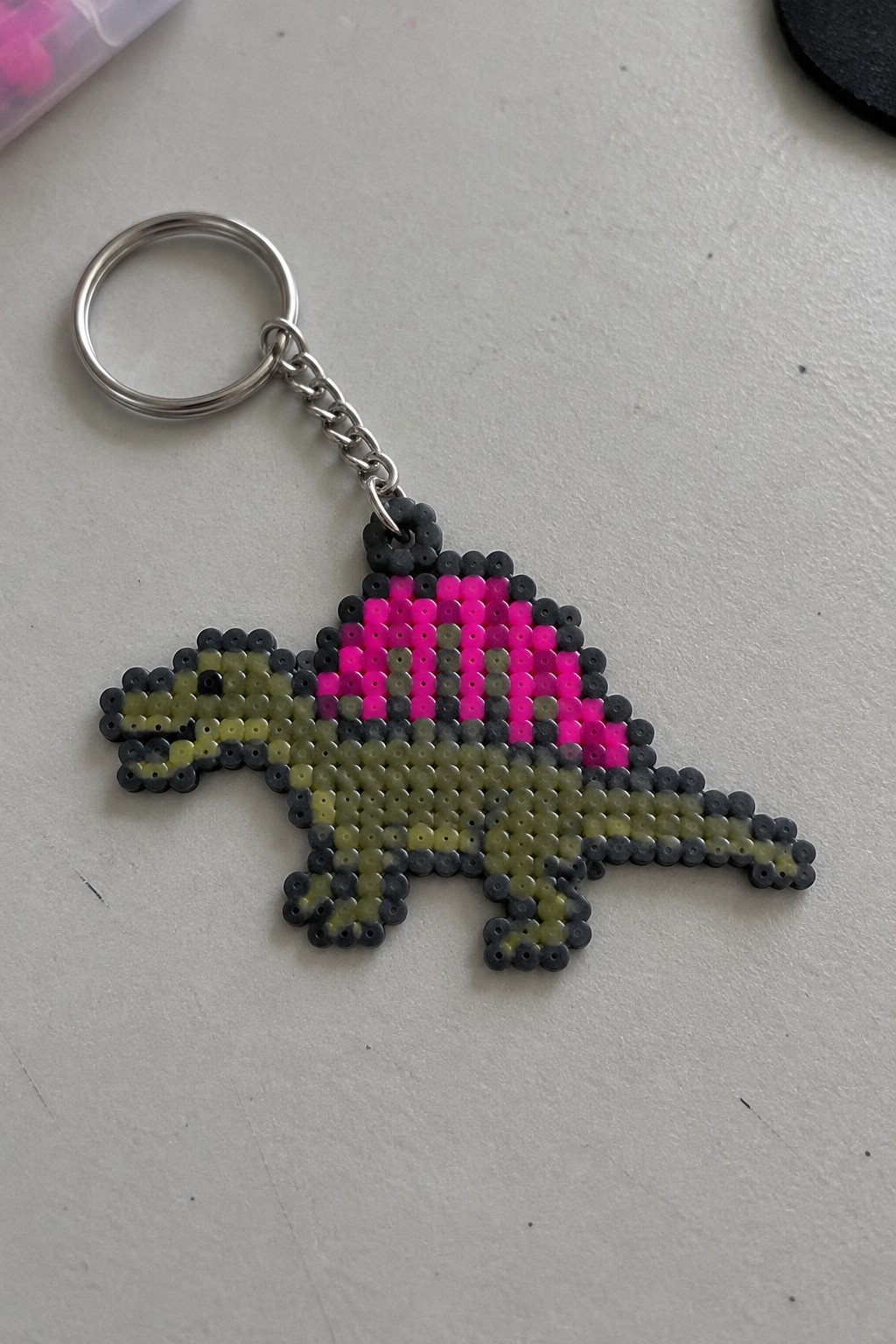 Perler bead stegosaurus keychain with green body, gray accents, and pink plates
