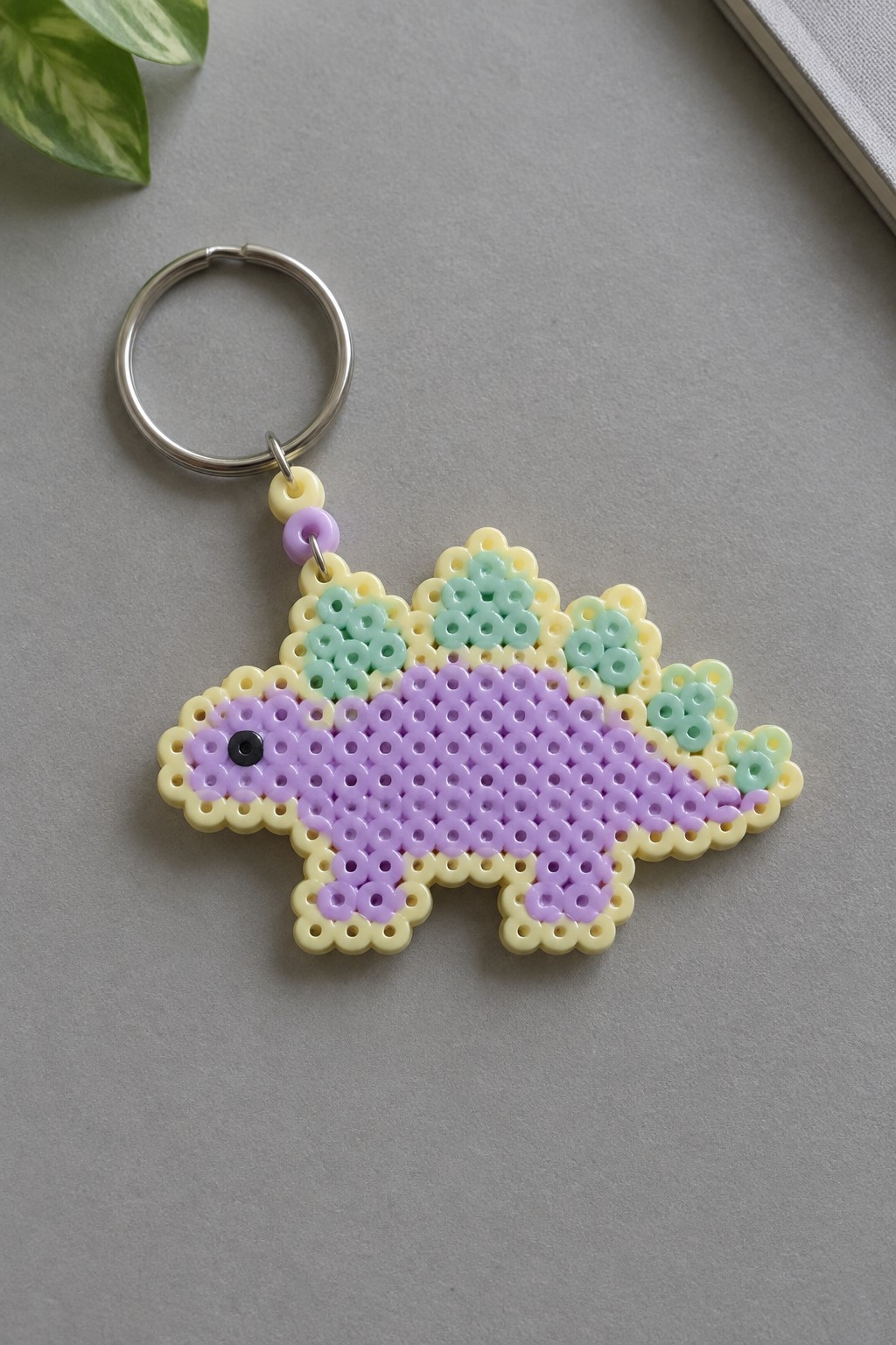 Pastel perler bead stegosaurus keychain with purple body, yellow border, and metal ring