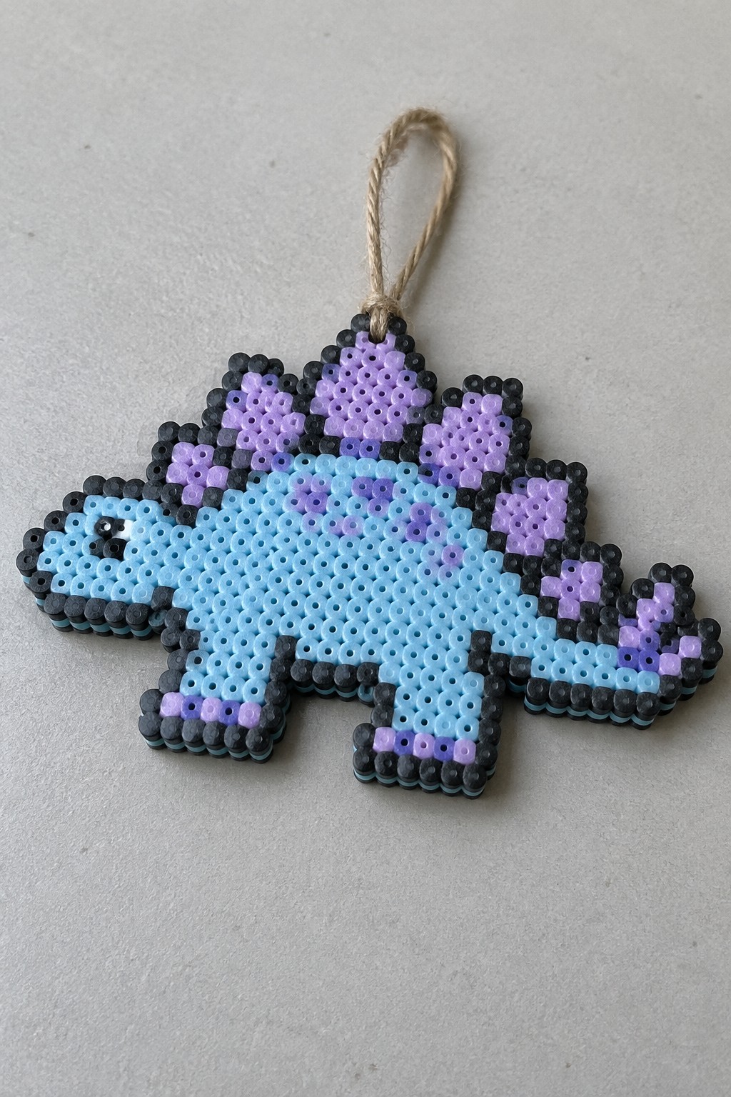 Blue perler bead dinosaur ornament with purple plates, black border, twine hanger