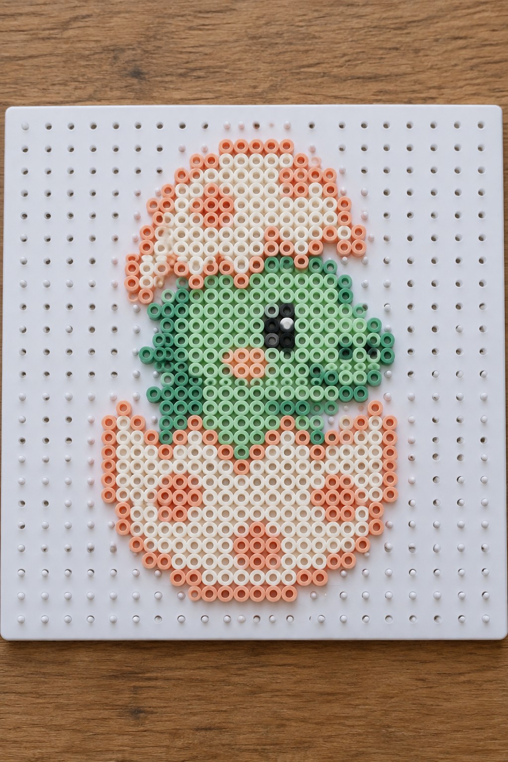 Green perler bead dinosaur hatching from orange egg wearing Santa hat