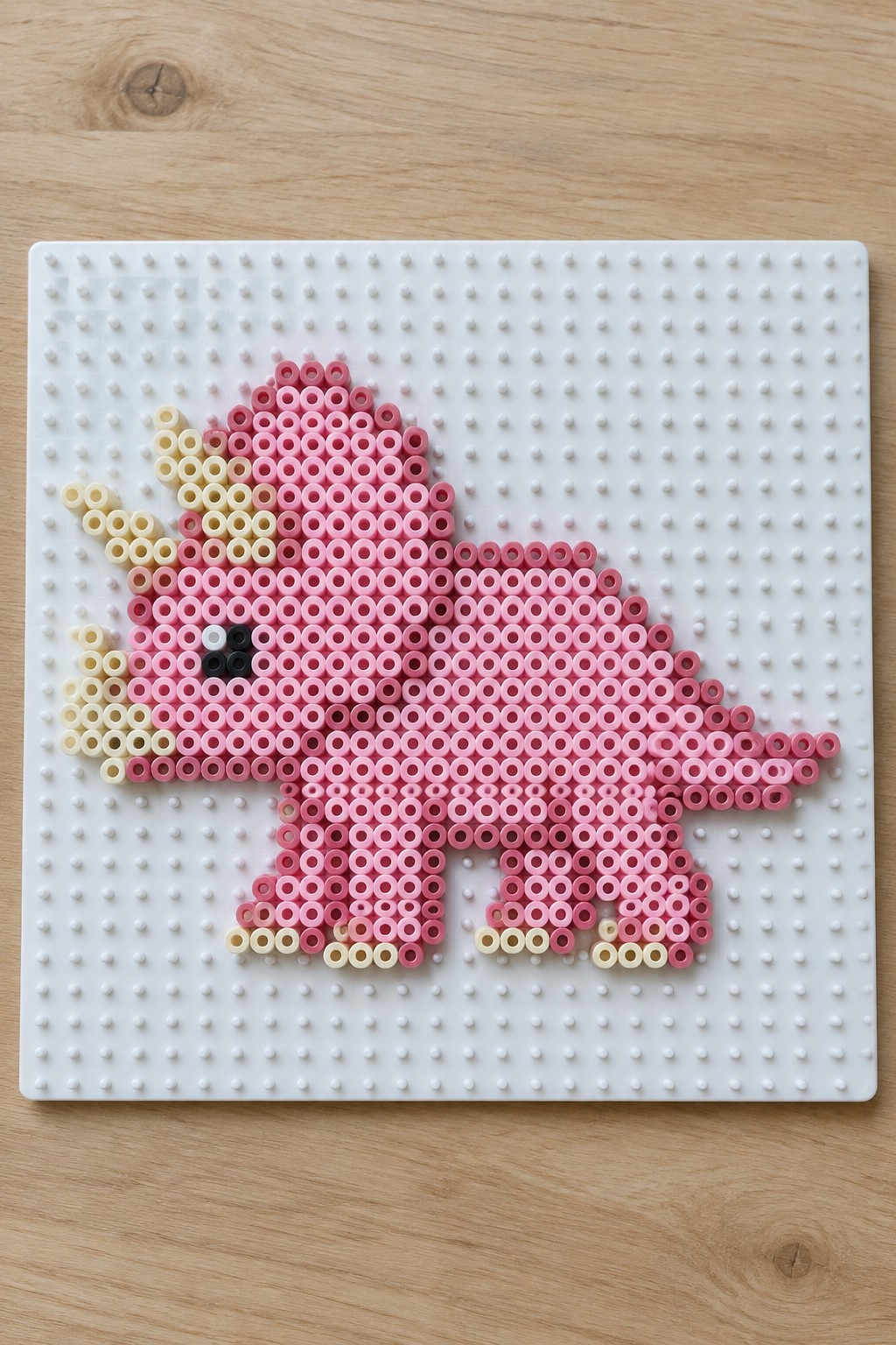 Pink perler bead dinosaur on white pegboard over wooden surface